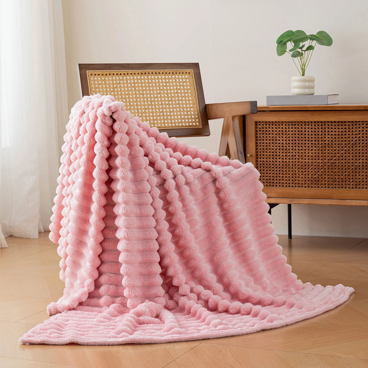 A fluffy pink brushed flannel throw blanket draped on a wooden table next to a plant.