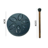 A dark gray mini steel tongue drum with six tuning holes and a wooden mallet shown next to a measurement scale.
