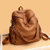 A tan leather backpack with rivets and drawstring closure resting on a light surface.