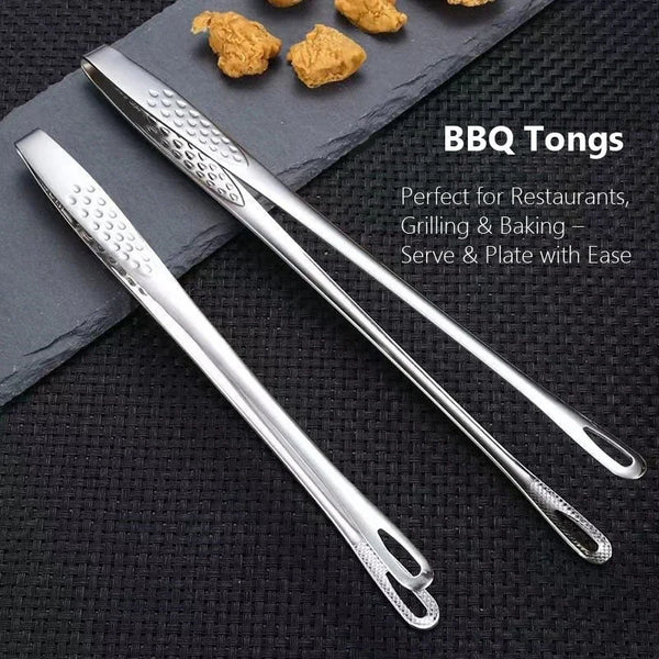 A pair of silver BBQ tongs resting on a dark slate surface with small pieces of food.
