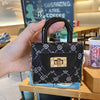 A black mini floral textured crossbody tote bag with a gold-toned padlock and chain is held in a hand.