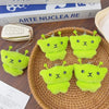 A set of cute green alien plush keychains with embroidered faces resting on a woven tray.