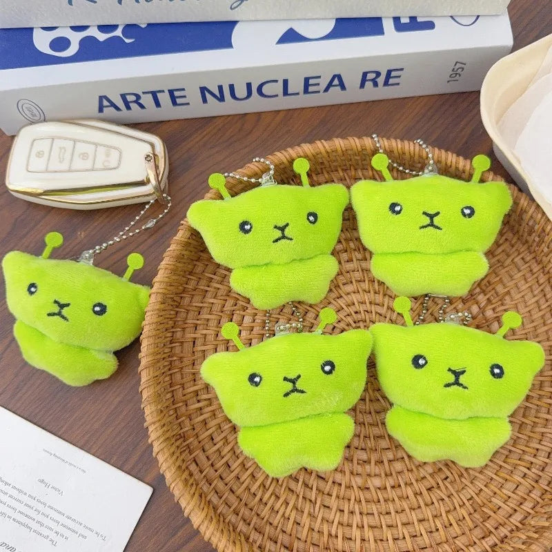 A set of cute green alien plush keychains with embroidered faces resting on a woven tray.