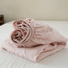 A light pink linen fitted sheet is rolled up on a white surface.