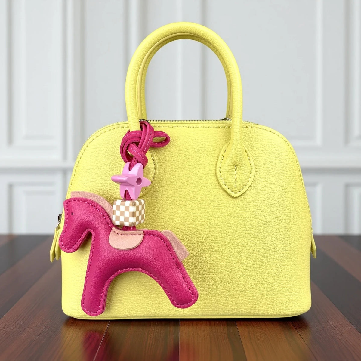 A yellow leather handbag with a pink pony charm and gold hardware sitting on a wooden surface.