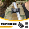 A silver hydration tube clip is shown attached to a green and brown backpack webbing strap.