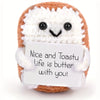 A handcrafted crocheted plush ornament shaped like a brown loaf with white icing and a small white tag.