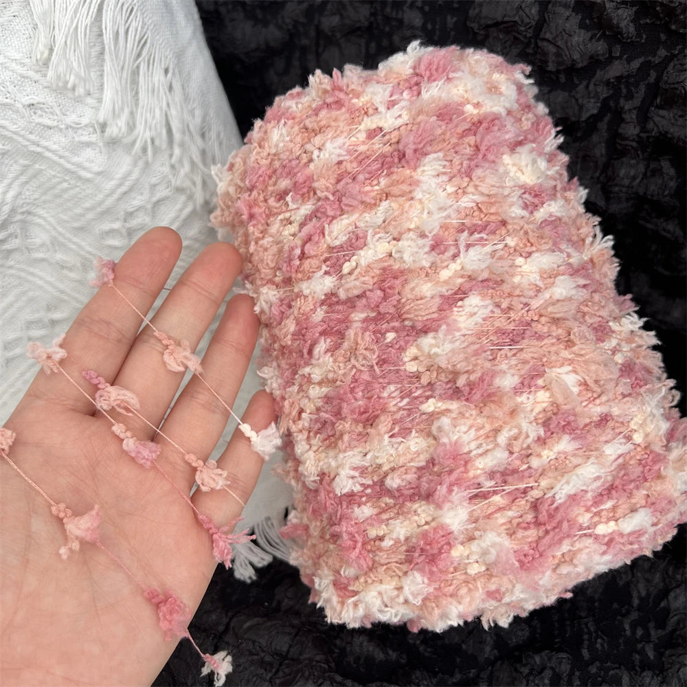 A hand holding a skein of pink and cream variegated cotton blend yarn for knitting and crochet.