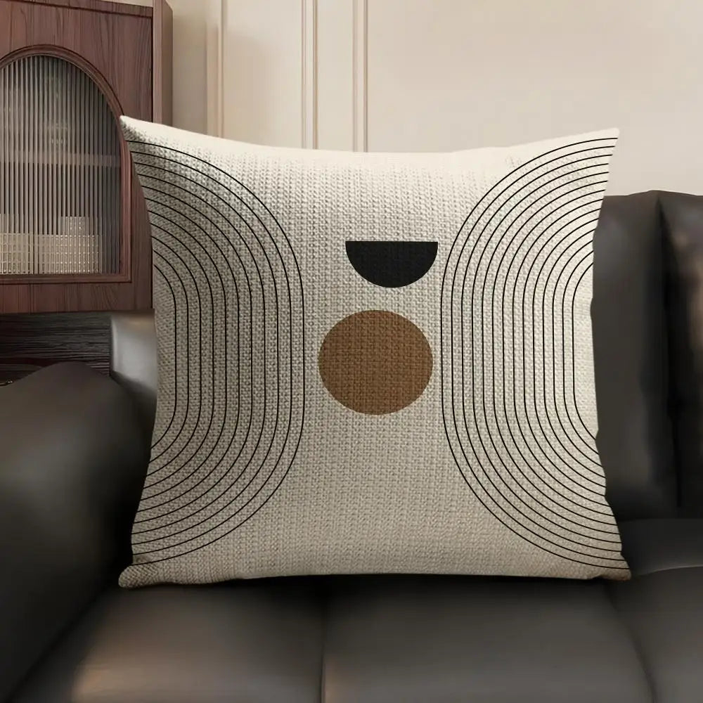 A beige cushion cover with black and tan concentric geometric lines on a dark leather sofa.