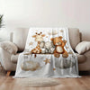 A white blanket featuring a print of a giraffe, an elephant, and a teddy bear on a light gray sofa.