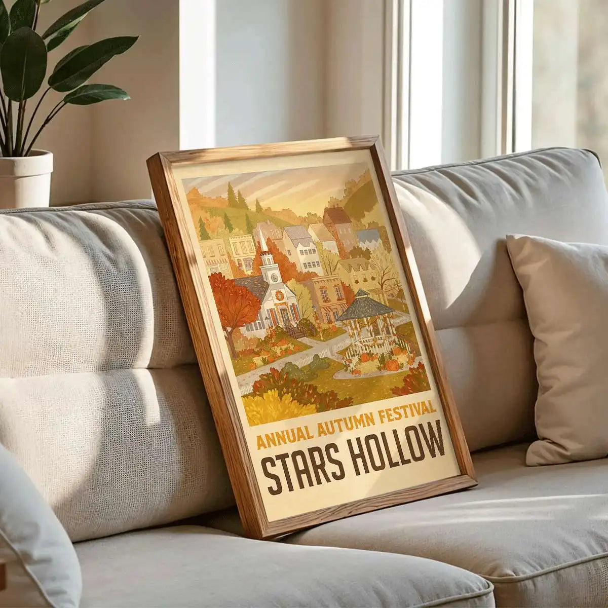 A framed canvas print depicting a village scene with autumn foliage and a market stall, displayed on a sofa.