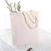 A light beige reusable canvas shopping tote bag with a natural fabric handle and sprigs of greenery, placed in a white wire b