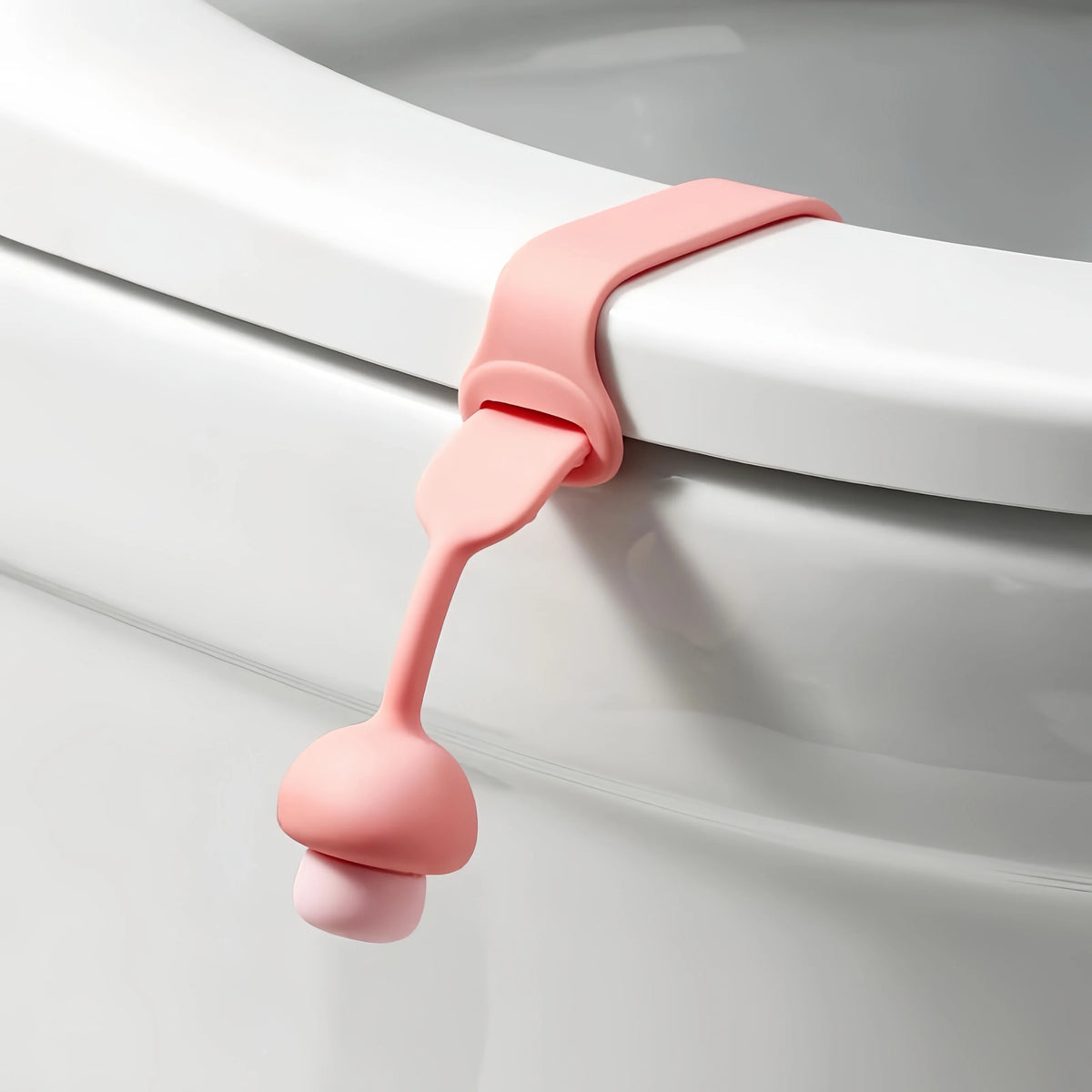 A pink silicone toilet seat lifter with a pull ring is shown attached to a white porcelain toilet bowl.