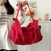 A bright red canvas travel tote bag with a black crossbody strap is being held by a person in a white shirt.