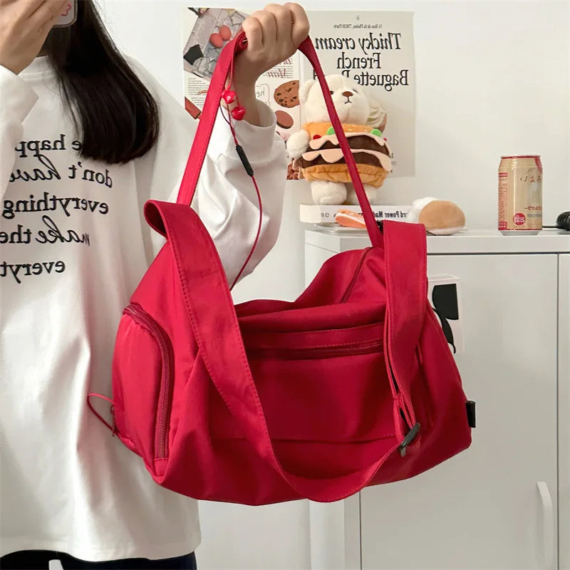 A bright red canvas travel tote bag with a black crossbody strap is being held by a person in a white shirt.