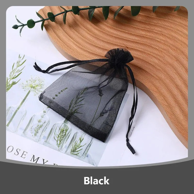 A black organza drawstring gift bag tied with a black ribbon, resting on a wooden surface next to greenery.