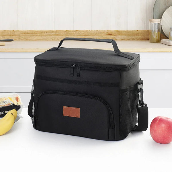 Black insulated leakproof tote bag resting on a white surface with fruit and wooden background.
