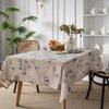 A beige cotton-linen tablecloth featuring a blue rustic fern print on a wooden table.