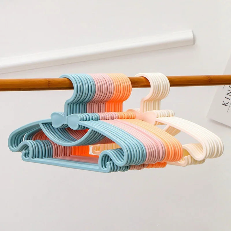 A set of colorful plastic hangers with bow designs hanging from a wooden rod.