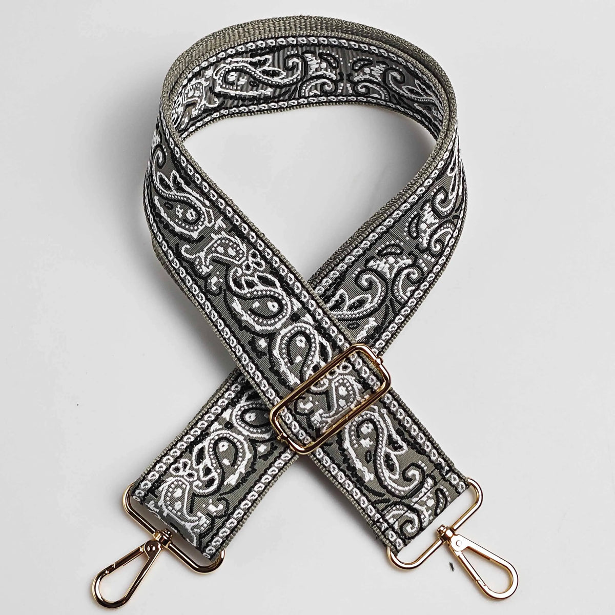 A close-up of an adjustable wide paisley jacquard bag strap in gray and white patterns.