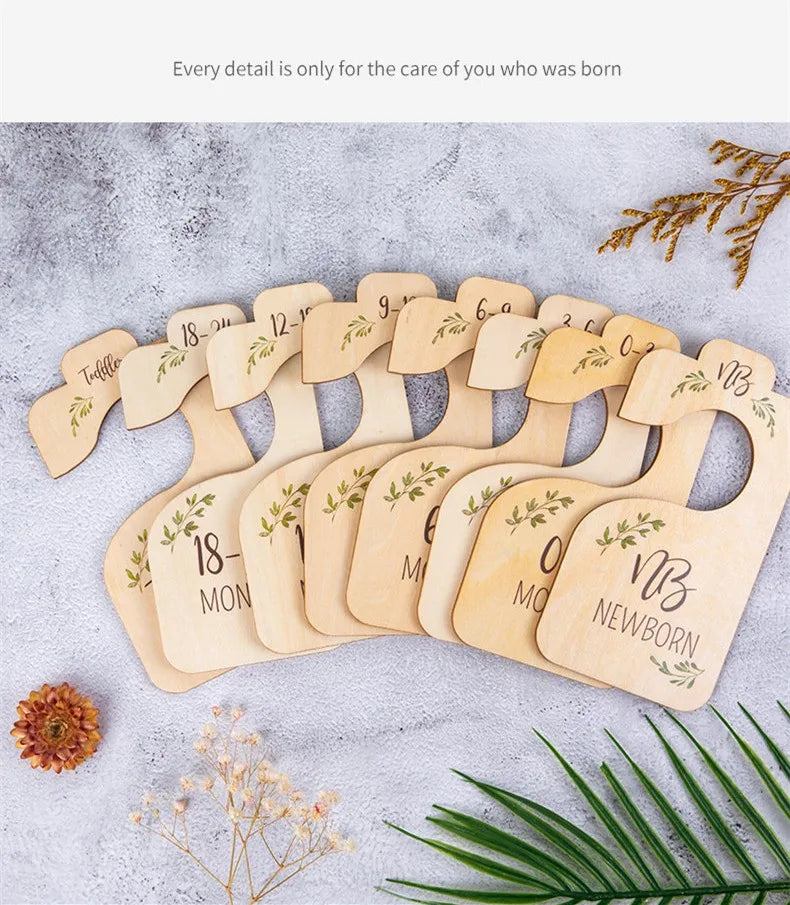 A set of eight wooden baby closet dividers showing sizes from newborn to 18 months, arranged on a gray surface.