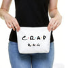 A person holds a white toiletry bag with black text that reads CRAP BAG.