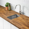 A kitchen countertop with a stainless steel sink and modern faucet set against white subway tile and wooden cabinetry.