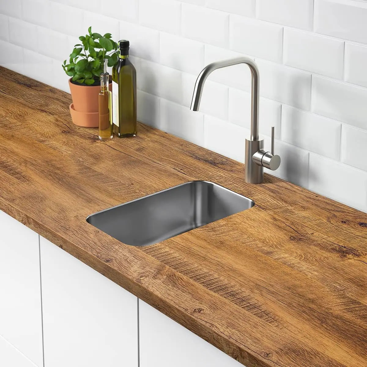 A kitchen countertop with a stainless steel sink and modern faucet set against white subway tile and wooden cabinetry.