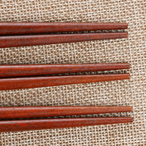A set of three reddish-brown wooden chopsticks laid diagonally on a woven burlap surface.