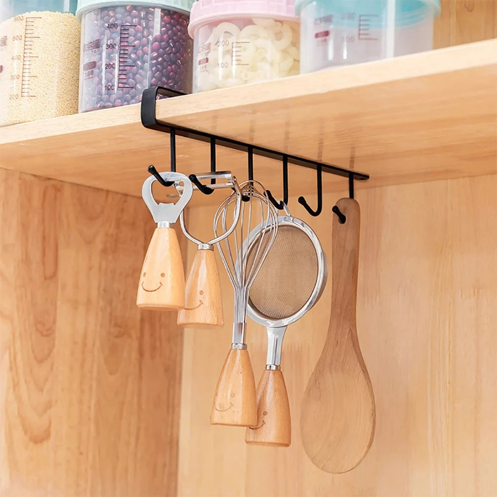 A wooden under-shelf cup and utensil holder with six hooks displaying various kitchen tools like whisks and spatulas.