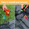 A hand installs a galvanized U-shaped garden staple into black landscape fabric with a green tool.