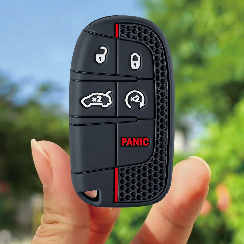 A hand holds a black silicone key fob cover with panic buttons for Jeep, Dodge, and Chrysler vehicles.