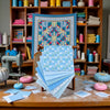 A bundle of light blue and white patterned cotton fabric squares for patchwork and quilting displayed on a wooden table.