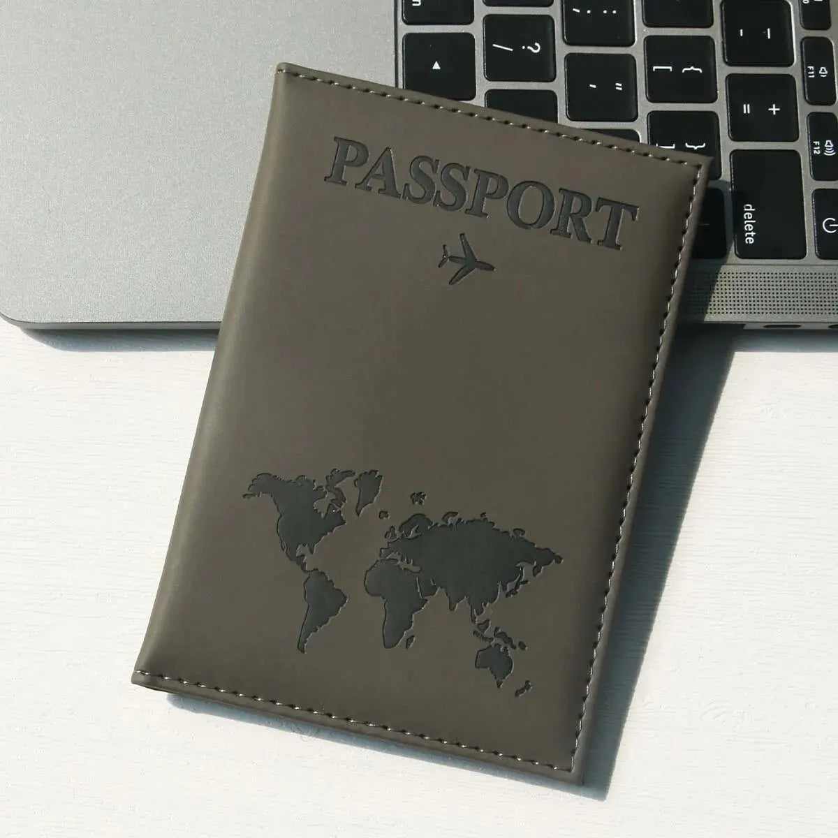 Braunes Leder-Reisepasshülle mit Weltkarten-Design auf weißer Oberfläche neben Laptop-Tastatur.