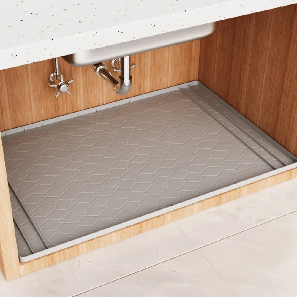 A silicone mat protecting the bottom of a kitchen sink cabinet, installed inside a wooden cabinet.