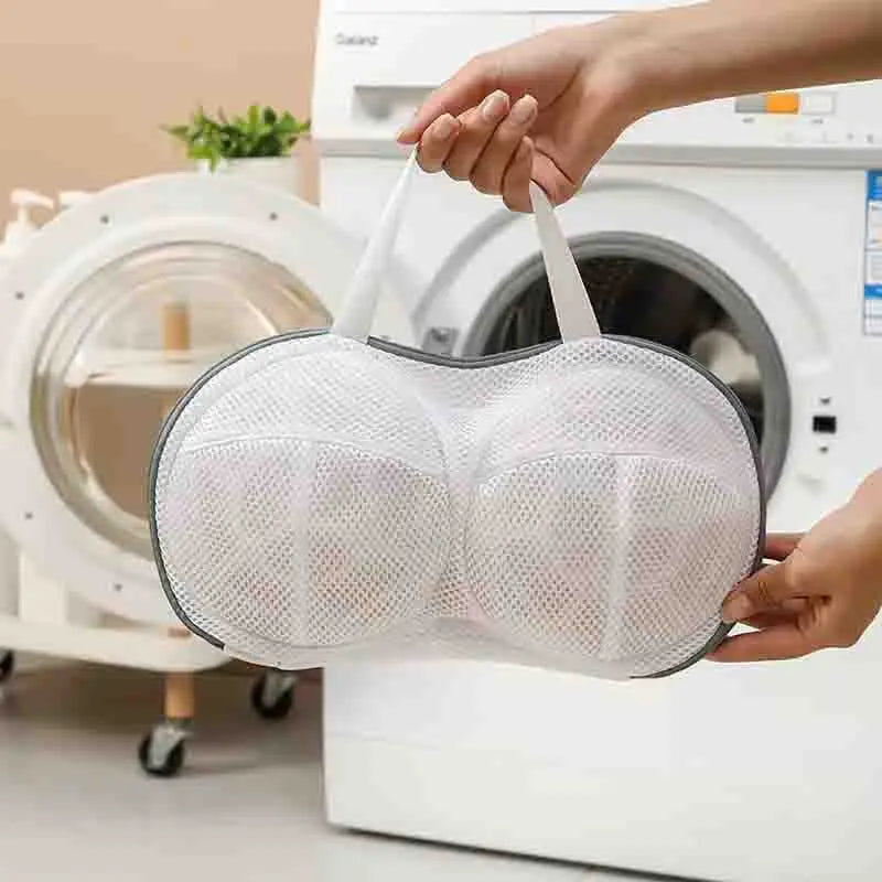 A hand is holding a white mesh laundry bag designed for bra protection near a washing machine.