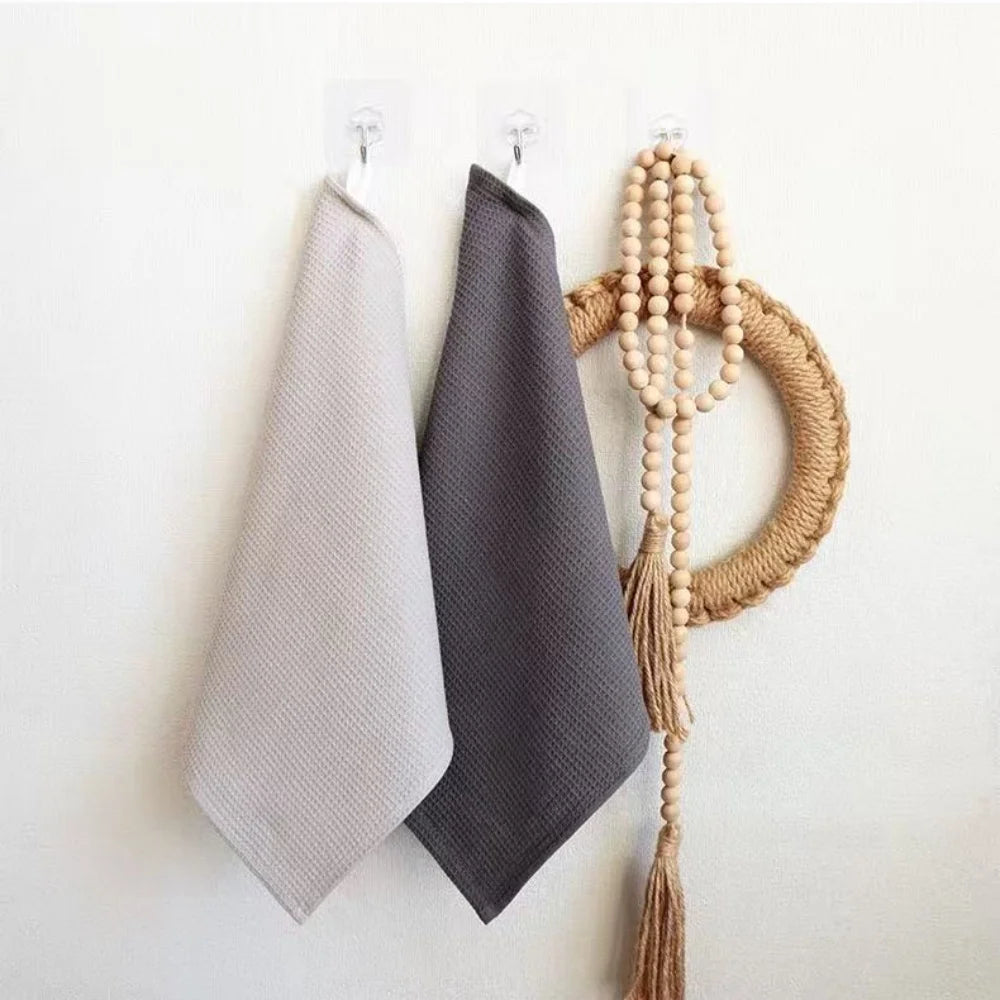 A set of four gray waffle weave towels hanging on a white wall next to a natural fiber macrame piece.