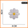 A white embroidered flower patch resembling a rose with a yellow center, shown against a measurement scale.