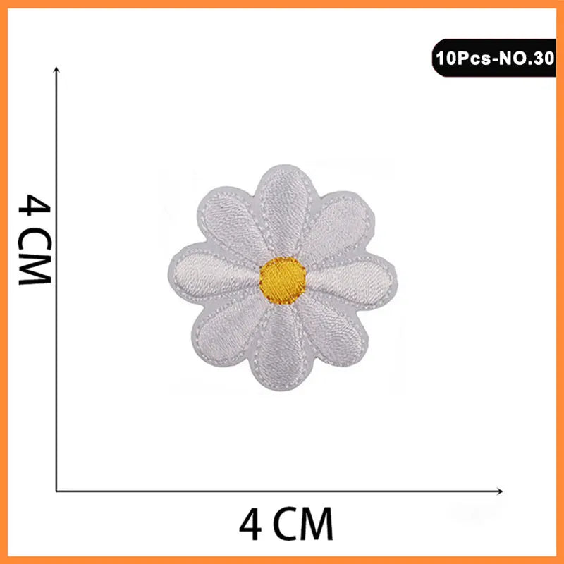 A white embroidered flower patch resembling a rose with a yellow center, shown against a measurement scale.