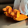 Two orange plush cartoon dachshund dogs wearing red and yellow collars resting on a dark surface.