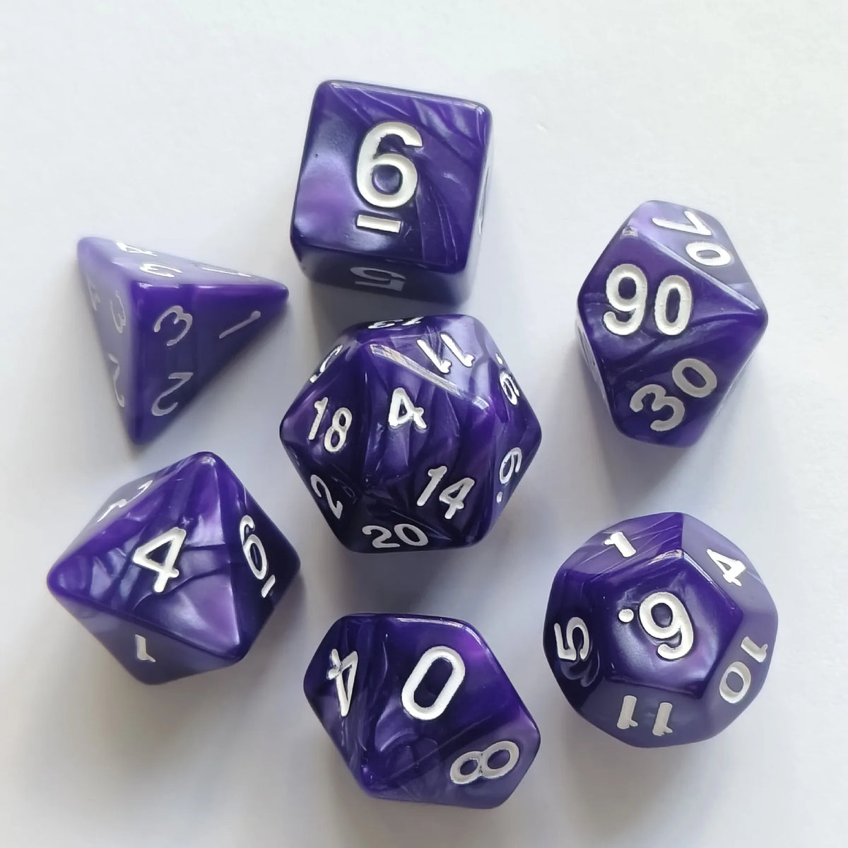 A collection of seven purple and white pearl pattern polyhedral dice scattered on a white surface.