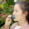 A young woman holds a blue harmonica in its protective case against a blurred green outdoor background.