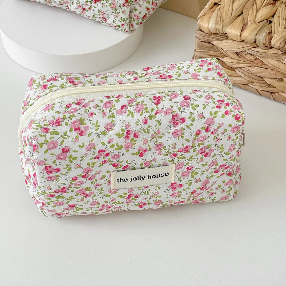A pink floral quilted makeup bag with a zipper closure resting on a white surface.