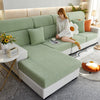 A light green elegant sofa slipcover with a white knitted sweater and orange accent pillows in a modern living room.