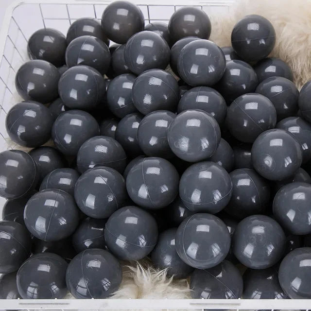 A large quantity of dark gray plastic ball pit balls are visible in a white basket.