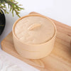 A light beige squishy stress relief toy set in a round container resting on a wooden cutting board.