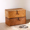 A rectangular woven rattan storage basket with a lid, made of natural brown material, resting on a wooden surface.