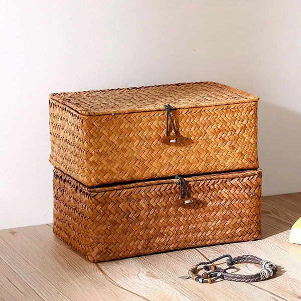 A rectangular woven rattan storage basket with a lid, made of natural brown material, resting on a wooden surface.