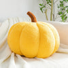 A bright yellow, fuzzy Halloween pumpkin plush pillow with a brown stem resting on a white knitted fabric.