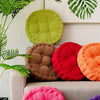 A collection of colorful thick corduroy floor cushions in green, brown, red, orange, and pink resting on a sofa.